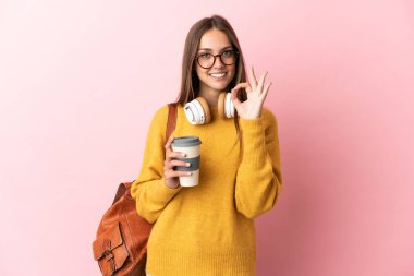 Tecrit edilmiş pembe arka plandaki genç bayan parmaklarıyla tamam işareti gösteriyor.