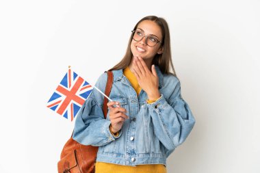 Young hispanic woman holding an United Kingdom flag over isolated white background looking up while smiling