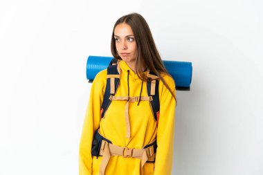 İzole edilmiş beyaz arka planda büyük bir sırt çantası olan genç dağcı kadın yan tarafa bakıyor.