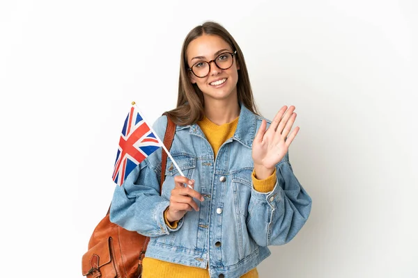 Young hispanic woman holding an United Kingdom flag over isolated white background saluting with hand with happy expression