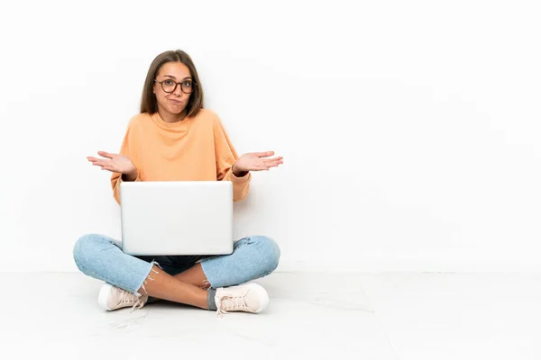 年轻女子 手持笔记本电脑坐在地板上疑惑不已 同时举手表决 — 图库照片