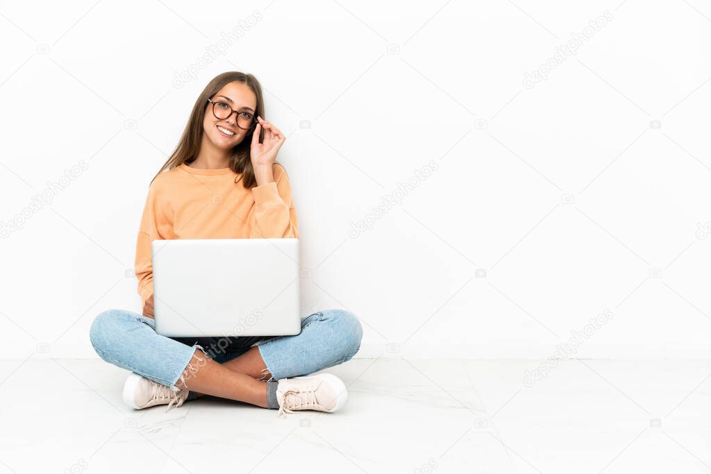 Young woman with a laptop sitting on the floor with glasses and happy