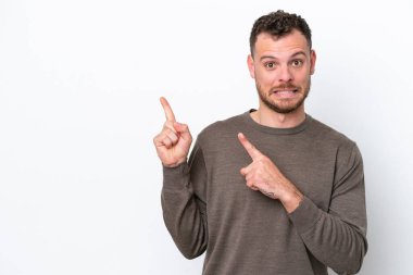Beyaz arka planda izole edilmiş genç Brezilyalı adam korkmuş ve kenarı işaret ediyor.