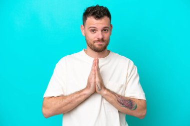 Mavi arka planda izole edilmiş genç Brezilyalı adam avuç içlerini bir arada tutuyor. İnsan bir şey ister.