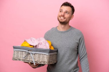 Genç Brezilyalı bir adam pembe arka planda izole edilmiş bir sepetle yukarı bakarken bir fikir düşünüyor.