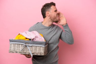 Genç Brezilyalı bir adam pembe arka planda izole edilmiş bir çamaşır sepeti tutuyor ve ağzı sonuna kadar açık bağırıyor.