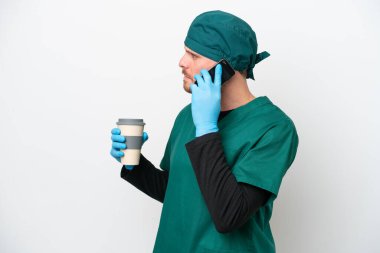 Cerrah Brezilyalı yeşil üniformalı adam beyaz arka planda izole edilmiş. Elinde kahve ve cep telefonu var.