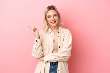 Pembe arka planda izole edilmiş genç beyaz kadın mutlu ve dik duruyor.