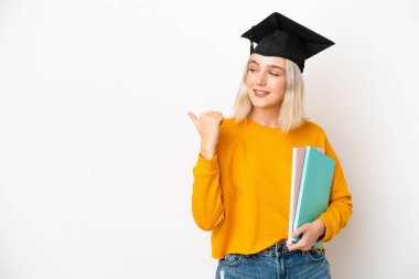 Beyaz arka planda izole edilmiş beyaz bir üniversite mezunu genç bir kadın bir ürün sunmak için kenarı işaret ediyor.