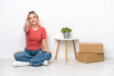 Young woman moving in new home among boxes isolated on white background shaking hands for closing a good deal