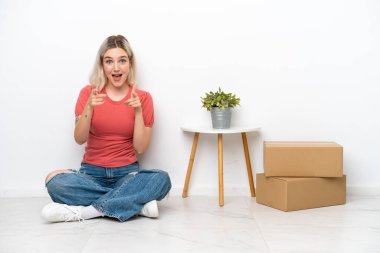 Young woman moving in new home among boxes isolated on white background pointing to the front and smiling