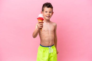Küçük beyaz bir çocuk pembe arka planda izole edilmiş, mutlu bir ifadeyle dondurma yiyor.