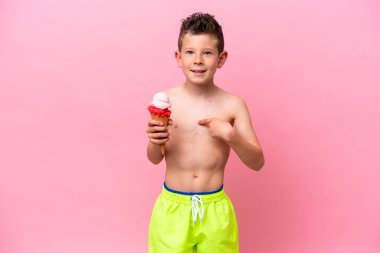 Küçük beyaz bir çocuk pembe arka planda izole edilmiş yüz ifadesiyle dondurma yiyor.