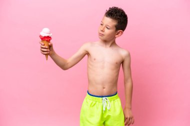 Küçük beyaz bir çocuk pembe arka planda izole edilmiş, mutlu bir ifadeyle dondurma yiyor.