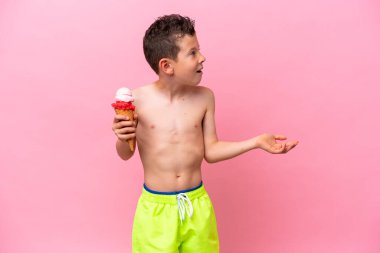 Küçük beyaz bir çocuk pembe arka planda izole edilmiş yüz ifadesiyle dondurma yiyor.