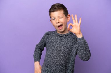 Little boy isolated on purple background showing ok sign with fingers