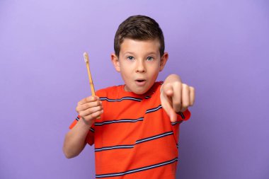 Mor arka planda dişlerini fırçalayan küçük çocuk şaşırmış ve ön tarafı işaret ediyor.