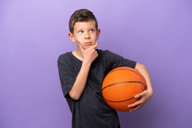 Little boy playing basketball isolated on purple background having doubts