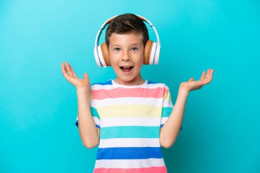 Little boy isolated on blue background surprised and listening music