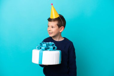 Küçük çocuk mavi arka planda izole edilmiş doğum günü pastası tutuyor.