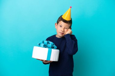 Elinde doğum günü pastası tutan küçük çocuk mavi arka planda izole edilmiş hayal kırıklığına uğramış ve kulaklarını kapatmış