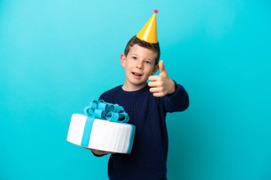 Küçük çocuk mavi arka planda izole edilmiş bir doğum günü pastası tutuyor. Başparmakları havada çünkü iyi bir şey oldu.