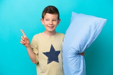 Mavi arka planda izole edilmiş pijamalı küçük çocuk harika bir fikre işaret ediyor.