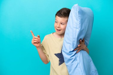 Mavi arka planda izole edilmiş pijamalı küçük çocuk parmağını kaldırarak çözümü bulmaya çalışıyor.