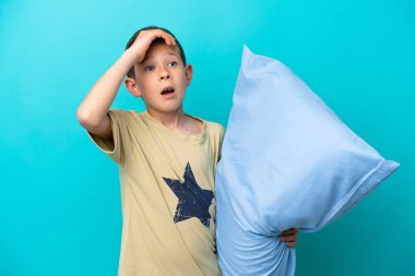 Mavi arka planda izole edilmiş pijamalı küçük çocuk yan tarafa bakarken sürpriz jest yapıyor.