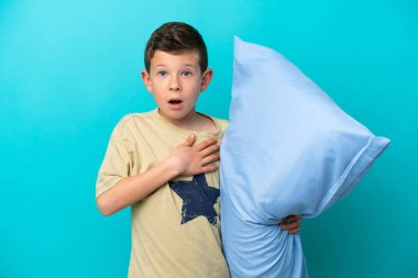 Mavi arka planda izole edilmiş pijamalı küçük çocuk sağa bakarken şaşırmış ve şok olmuştu.