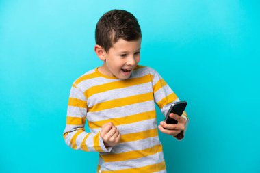 Küçük çocuk mavi arka planda cep telefonu kullanarak ve zafer jesti yaparak izole edildi.