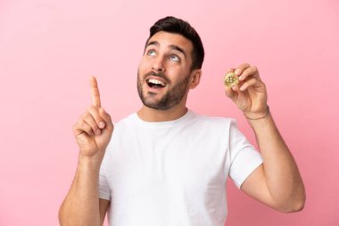Elinde pembe arka planda izole edilmiş Bitcoin tutan genç adam harika bir fikre işaret ediyor.