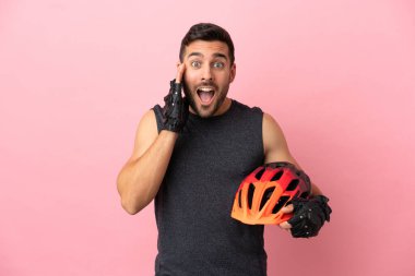 Genç bisikletçi, pembe arka planda izole edilmiş, şaşırmış ve şok olmuş bir yüz ifadesi var.