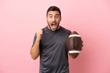 Pembe arka planda ragbi oynayan beyaz bir adam galibiyetini kutluyor.