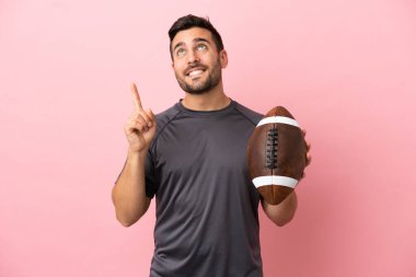 Genç beyaz adam pembe arka planda izole edilmiş rugby oynuyor. Harika bir fikre işaret ediyor.