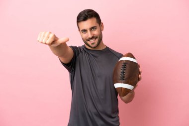 Pembe arka planda ragbi oynayan genç beyaz bir adam baş parmak hareketi yapıyor.