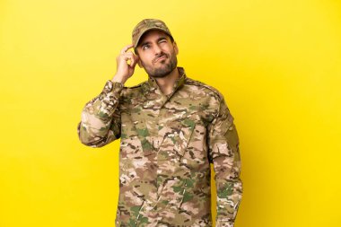 Sarı arka planda izole edilmiş askerin şüpheleri ve kafası karışmış yüz ifadesi var.