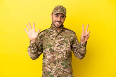 Military man isolated on yellow background counting seven with fingers