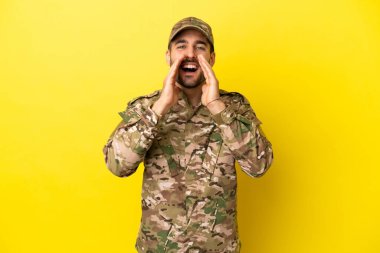 Military man isolated on yellow background shouting and announcing something