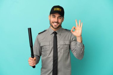 Mavi arka planda izole edilmiş genç güvenlik görevlisi parmaklarıyla işaret gösteriyor.
