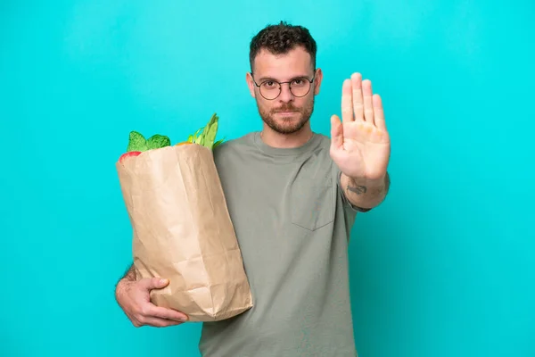 Young Brazilian Man Holding Grocery Shopping Bag Isolated Blue Background — Φωτογραφία Αρχείου