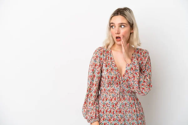 Beyaz arka planda izole edilmiş genç beyaz kadın yan tarafa bakarken sürpriz bir jest yaparak bir şeyler fısıldıyor.