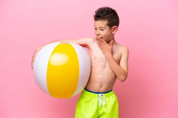 一个高加索小男孩拿着一个海滩球 被粉色背景隔开 脸上带着惊讶和震惊的表情 — 图库照片