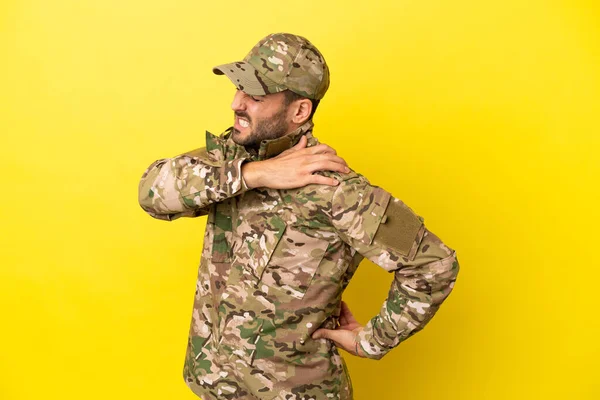 Military man isolated on yellow background suffering from pain in shoulder for having made an effort