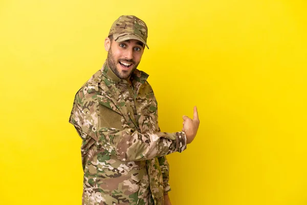 Military man isolated on yellow background pointing back