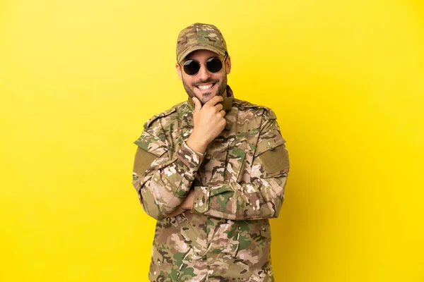 Military man isolated on yellow background with glasses and smiling