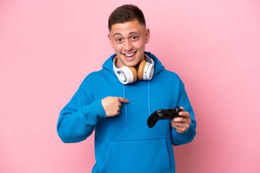 Pembe arka planda izole edilmiş bir bilgisayar oyunu kontrolörüyle oynayan Brezilyalı genç bir adam.