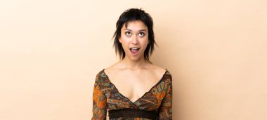 Hintli kadın bej arka planda izole edilmiş yukarı bakıyor ve şaşırmış bir ifadeyle