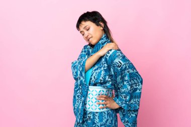 Kimono giyen genç bir kadın, izole edilmiş mavi arka plan üzerinde çabaladığı için omzunda ağrıdan muzdarip.