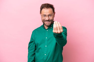 Orta yaşlı, beyaz bir adam pembe arka planda izole edilmiş, bizimle gelmesi için davet ediliyor. Gelmene sevindim.